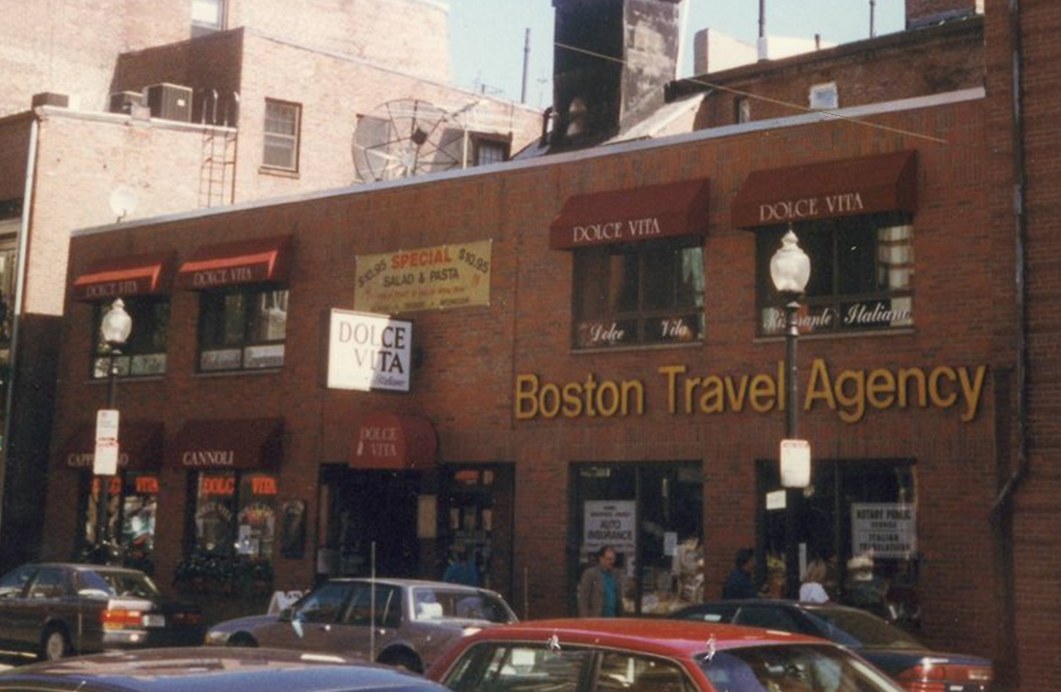 Color photo of the second Boston Travel Agency office, a brick storefront with gold lettering on a North End street